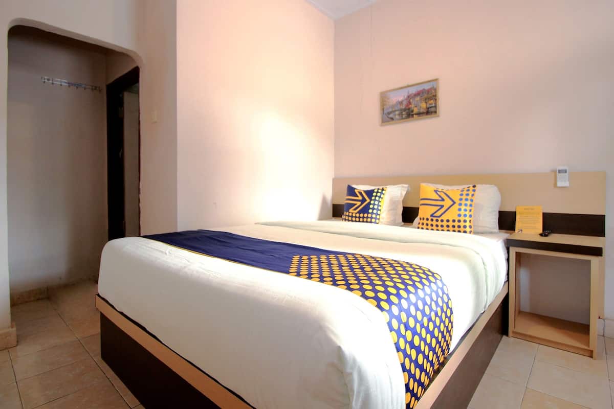 A hotel room with a bed, a nightstand, a painting on the wall, and a door.