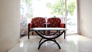 Un coin repas avec une table et des chaises à plateau en verre, une étagère blanche et une vue sur la rue à travers une porte vitrée.
