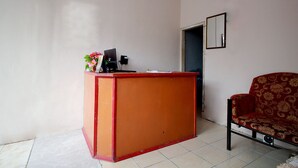 Une pièce avec un bureau rouge et orange, une chaise noire, un miroir au mur et une porte donnant sur une autre pièce.