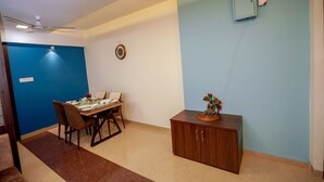A dining area with a table set for four, a ceiling fan, and a wall-mounted electrical box. - StayEden - Gracia Heights - 2 BHK (Indore)