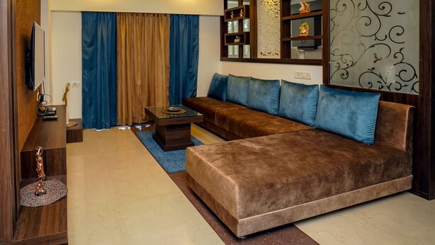 A modern living room with a brown sofa, blue cushions, a glass coffee table, and decorative shelves. - StayEden - Gracia Heights - 2 BHK (Indore)
