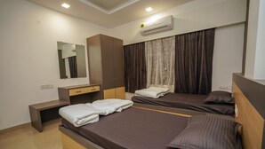 A hotel room with two beds, a wardrobe, a desk, a mirror, an air conditioning unit, and a window with curtains. - StayEden - Gracia Heights - 2 BHK (Indore)