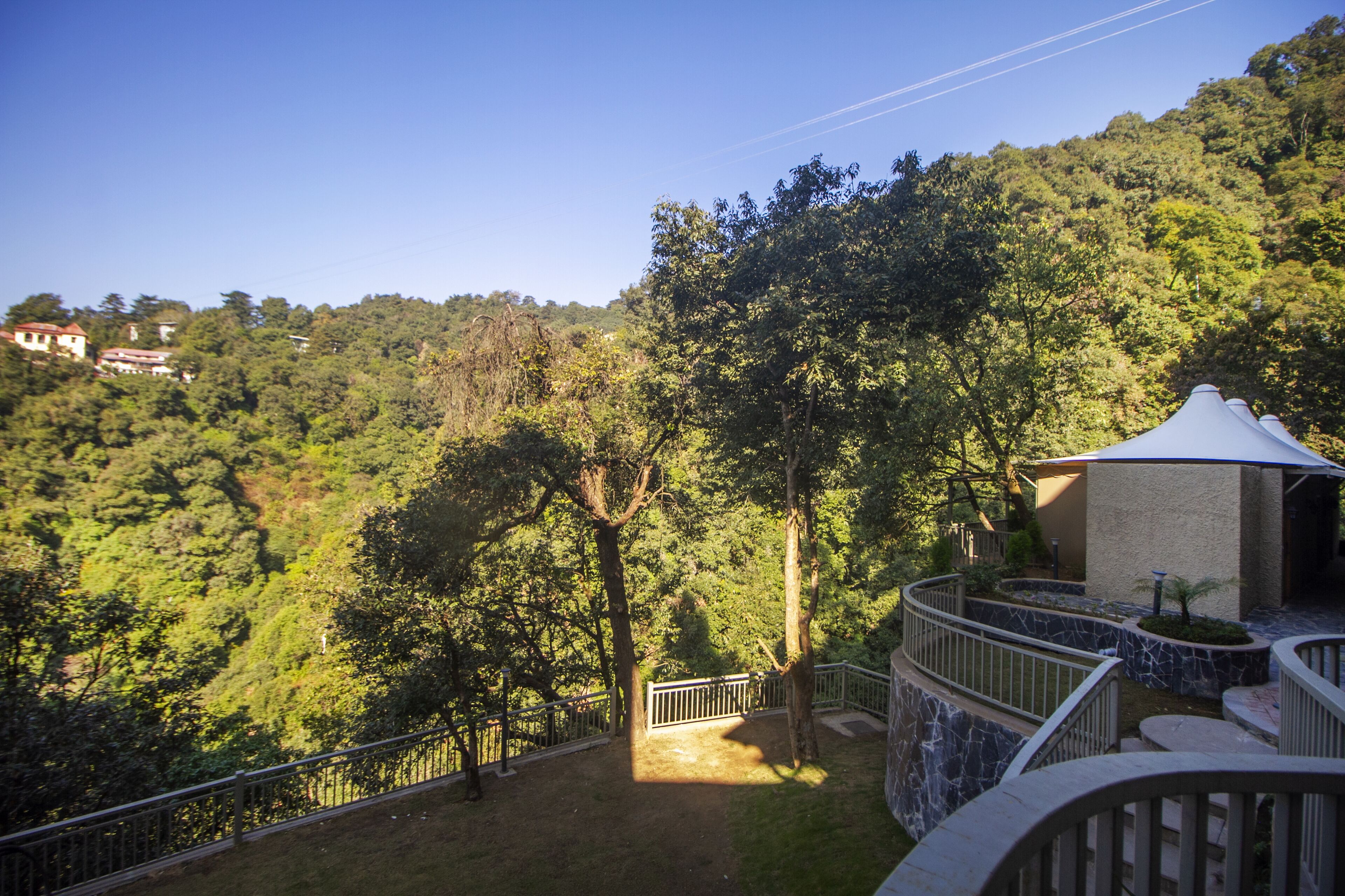 A view of a lush green hillside with a pathway leading to a building with a white roof.