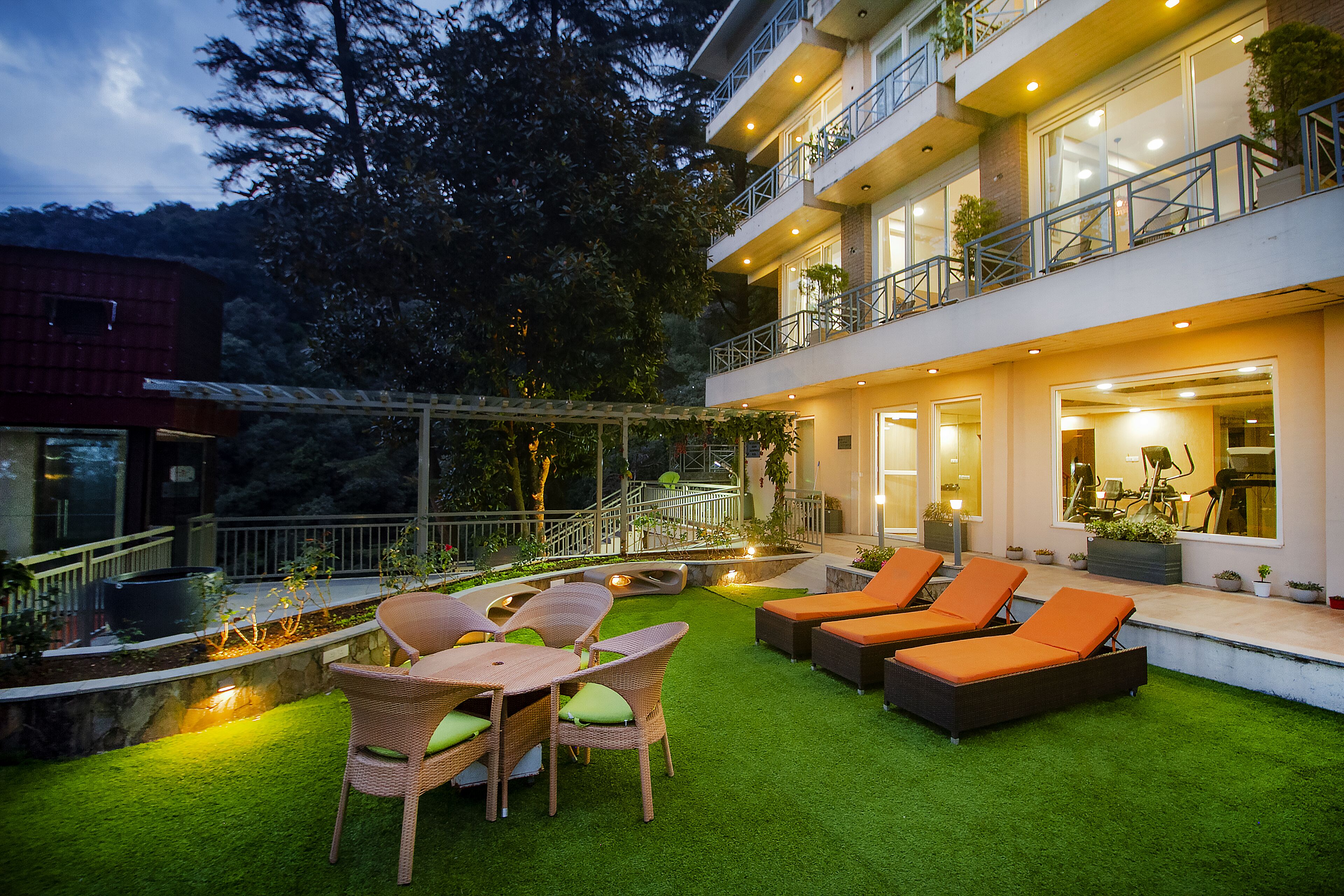 A modern outdoor patio with artificial grass, wicker furniture, and orange lounge chairs.