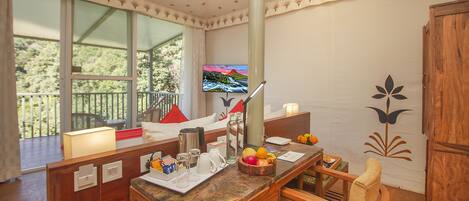 Una habitación con un escritorio de madera, televisor y un balcón con vistas a árboles.