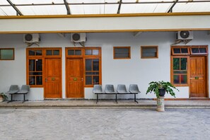 A building with multiple wooden doors and windows, a row of chairs, and a potted plant. - OYO 2737 D'KostNearKraton mangkunegaran (Surakarta)