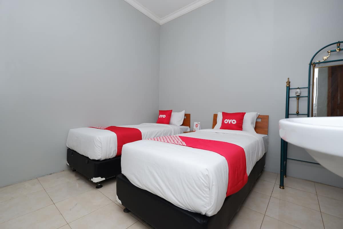 A hotel room with two beds, each with white bedding and red accents, a wooden headboard, and a small bedside table.