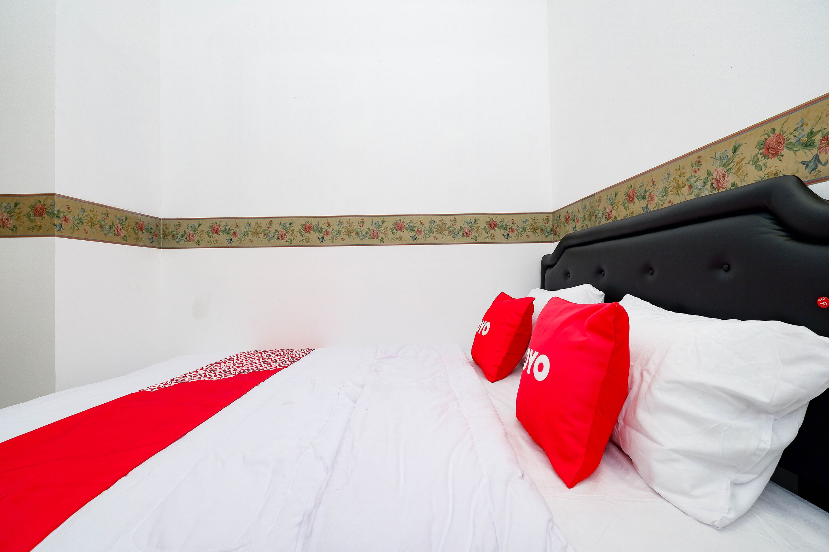 Een hotelkamer met een bed, rode en witte kussens en een bloemenrand aan de muur.