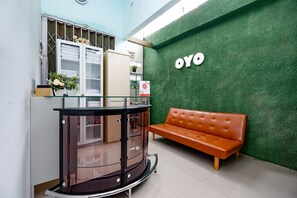 Un área de recepción con una pared verde, una barra de vidrio, un sofá marrón y una ventana con persianas.