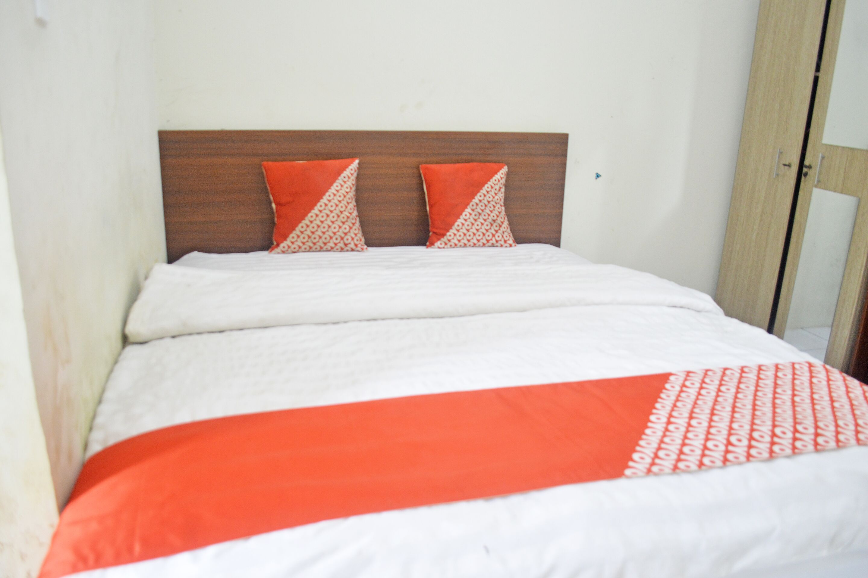 Una cama con cabecera de madera, ropa de cama blanca y dos almohadas naranjas.