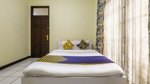 A neatly made bed with a patterned bedspread, two pillows with geometric designs, and a door with a small window. - Super OYO 2672 Bee M Syariah (Bandung)
