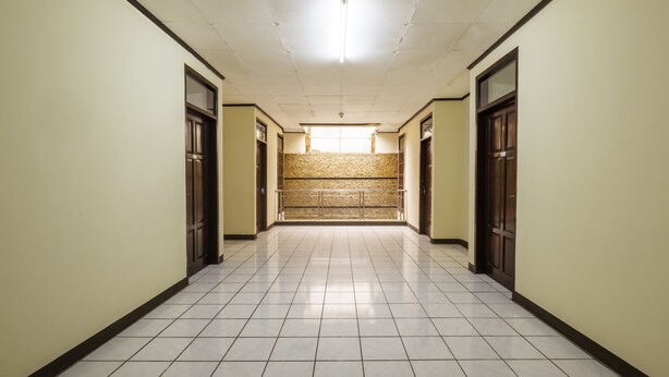 A long, narrow hallway with tiled floors and cream-colored walls, leading to a staircase. - Super OYO 2672 Bee M Syariah (Bandung)