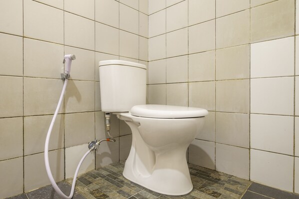 A toilet with a white tank and seat, a white hose, and a tiled floor with a mix of square and rectangular tiles. - Super OYO 2672 Bee M Syariah (Bandung)
