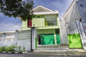 Un edificio de dos pisos con fachada verde, entrada protegida por una verja y una señalización visible.