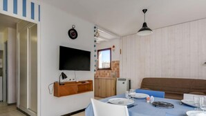 Un coin repas avec une table dressée pour deux personnes, un téléviseur fixé au mur et un meuble en bois en dessous.
