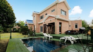 Une maison à deux étages, construite en briques, dotée d’une piscine, d’un espace salon extérieur et d’un patio couvert.