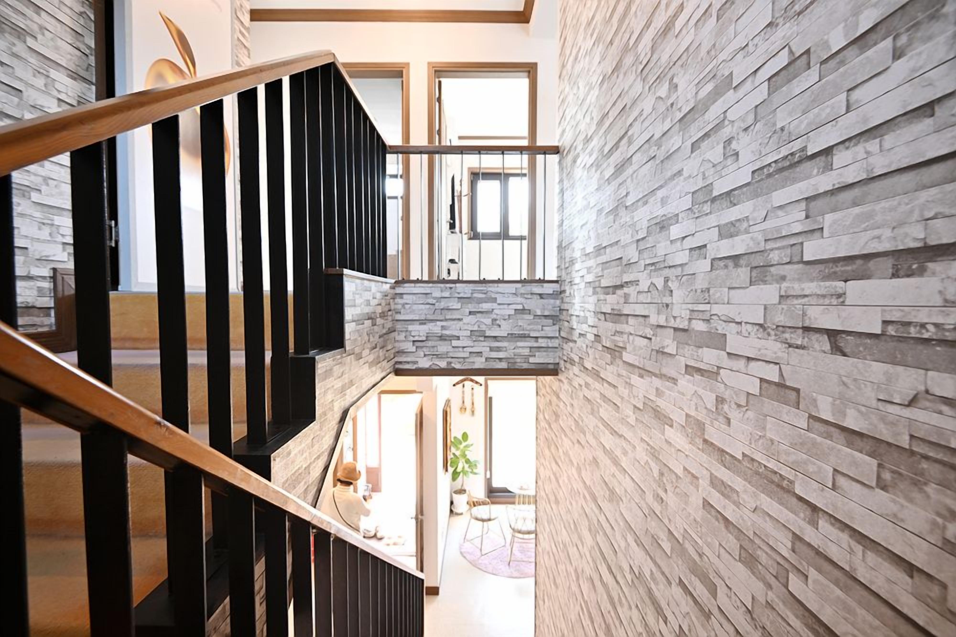 A modern interior with a staircase, stone wall, and a view into a dining area.