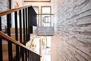 Interior moderno com escada, parede de pedra e vista para uma área de refeições.