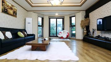 A spacious living room with a dark sofa, a white coffee table, and a large window offering a view of trees.