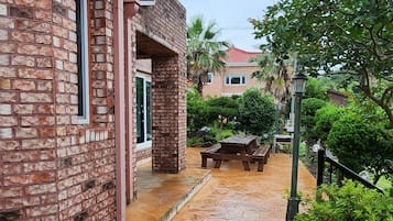 A brick pathway leading to a building with a balcony, surrounded by greenery and a patio area.