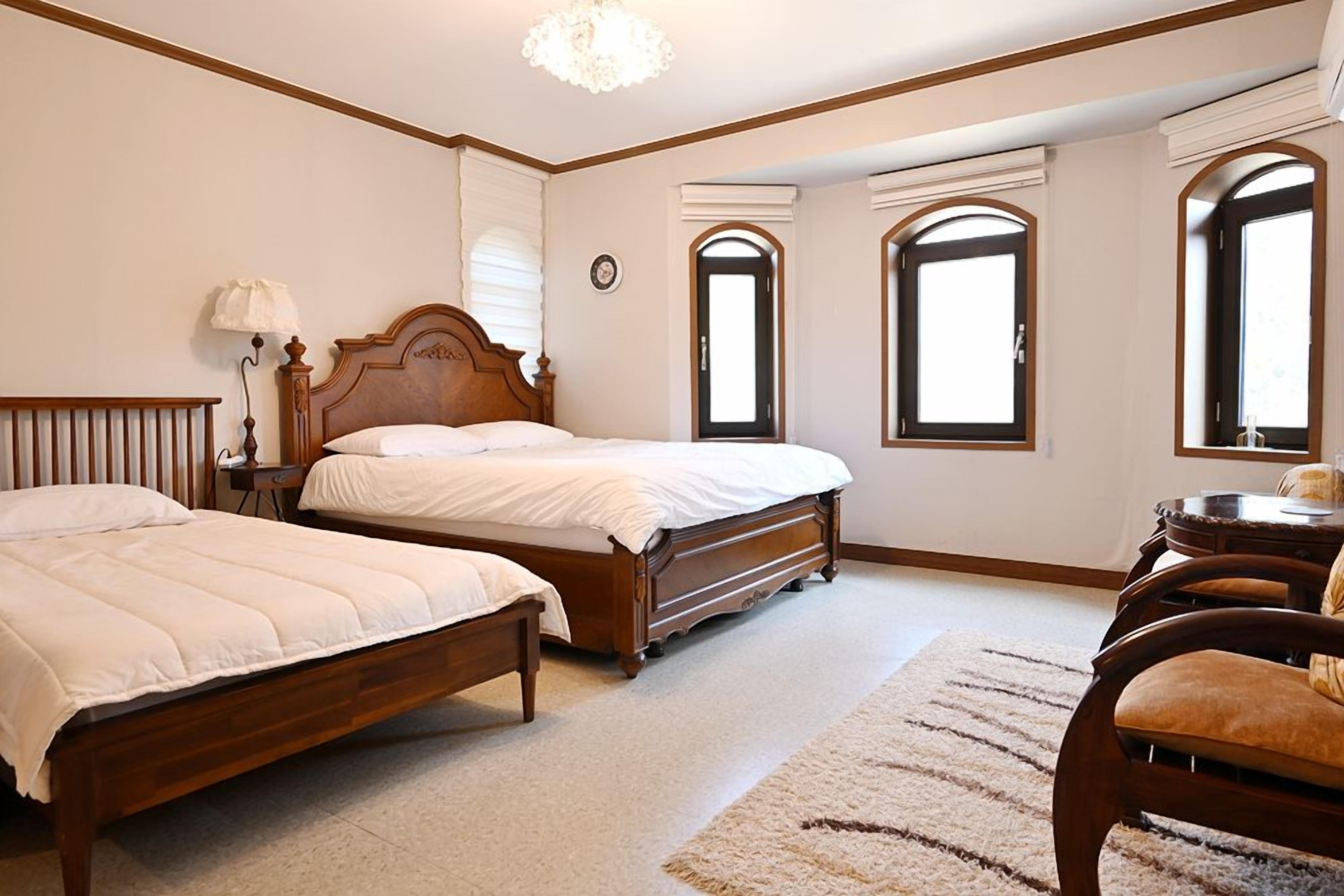Un dormitorio con dos camas de madera, una mesita de noche, una lámpara y una silla.