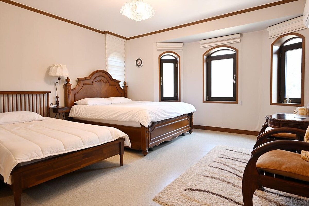 A bedroom with two wooden beds, a nightstand, a lamp, and a chair.