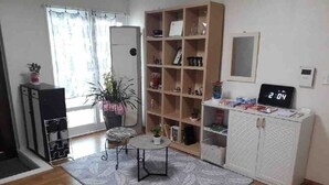 A room with a wooden floor, a bookshelf, a small table with a chair, a white cabinet, and a digital clock displaying 2:04. - Gwangju Songjeong Station Guesthouse - Hostel (Gwangju)