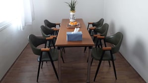 A dining area with a wooden table, six green chairs, a vase with a plant, and a tray with oranges and a tissue box. - Gwangju Songjeong Station Guesthouse - Hostel (Gwangju)