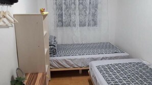 A small, neatly organized bedroom with two beds, a wooden wardrobe, a small table, and a potted plant. - Gwangju Songjeong Station Guesthouse - Hostel (Gwangju)