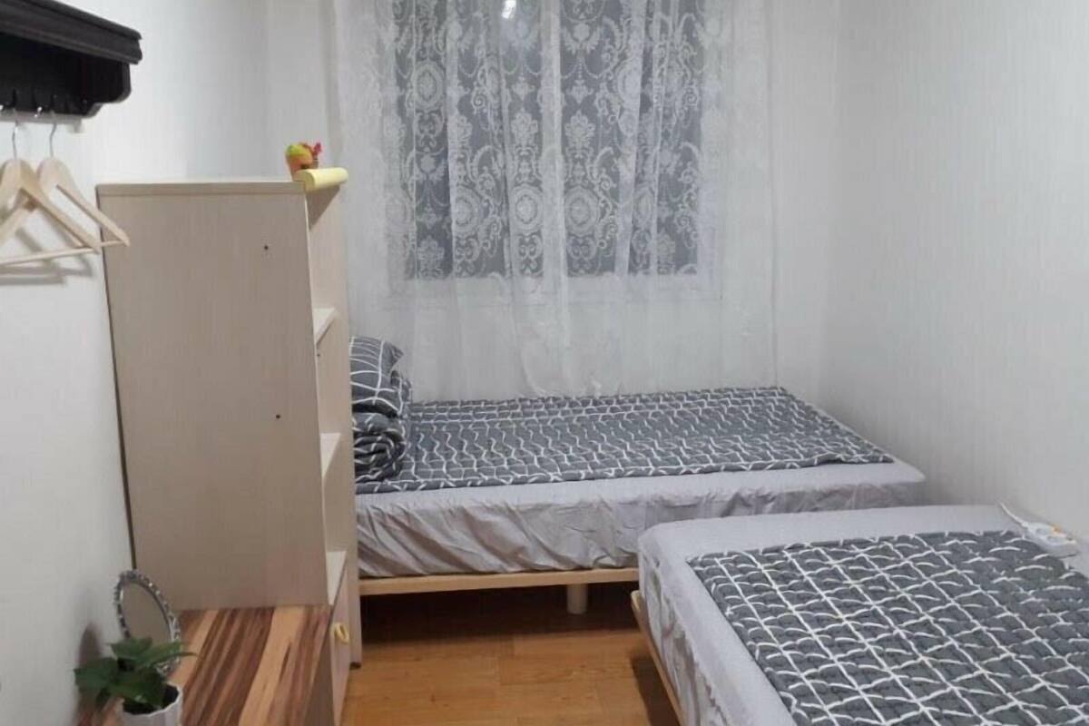 A small, neatly organized bedroom with two beds, a wooden wardrobe, a small table, and a potted plant.