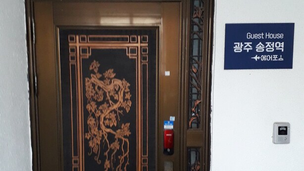 A door with intricate floral carvings, a fire alarm, and a sign indicating a guest house. - Gwangju Songjeong Station Guesthouse - Hostel (Gwangju)