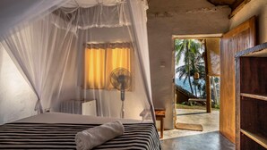 A bedroom with a bed, a bedside fan, and a view of the outdoors. - Sea View Clay House Dikwella (Dikwella)