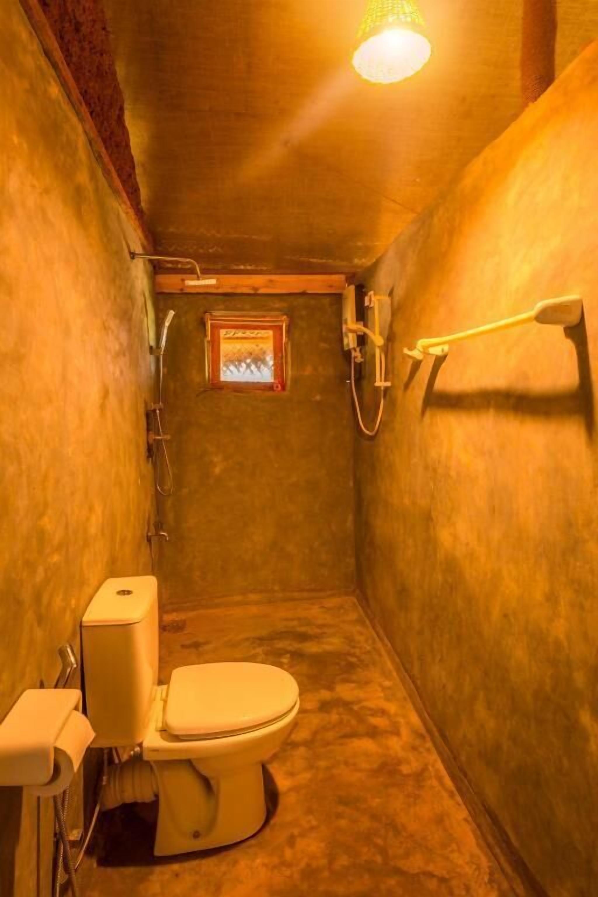 A small, narrow bathroom with a toilet, shower, and a small window.