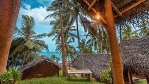 A tropical resort with thatched-roof huts, palm trees, and a bench in a lush garden setting. - Sea View Clay House Dikwella (Dikwella)