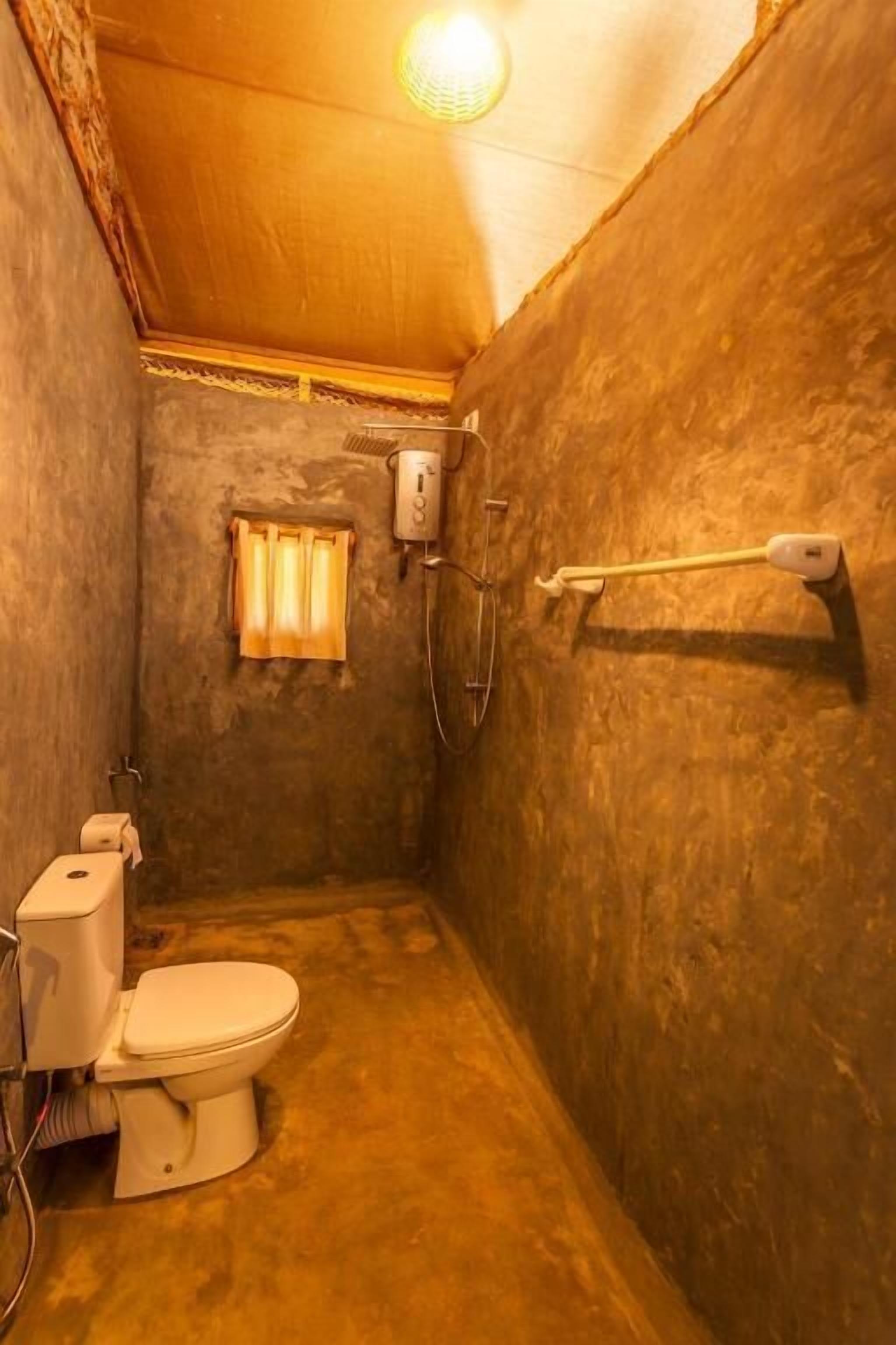 A small, compact bathroom with a toilet, a towel rack, and a shower head.