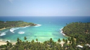 A tropical beach with clear turquoise waters, palm trees, and a rocky outcrop. - Sea View Clay House Dikwella (Dikwella)