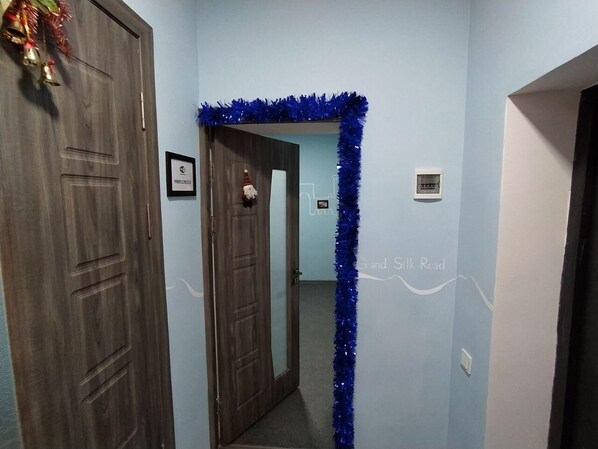 Un couloir avec une porte en bois sur la gauche, une décoration scintillante bleue et un tableau encadré accroché au mur.