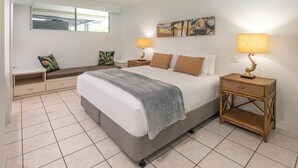 A bedroom with a bed, two bedside tables with lamps, a bench, and a wall-mounted artwork.