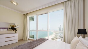 A hotel room with a large bed, a dresser, a mirror, and a view of a beach and cityscape.