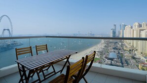 A balcony with a table and chairs overlooking a beach and cityscape.