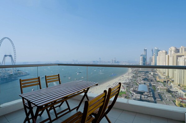 A balcony with a table and chairs overlooking a beach and cityscape.
