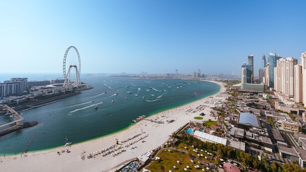 A coastal cityscape with a prominent Ferris wheel, a beach, and high-rise buildings.