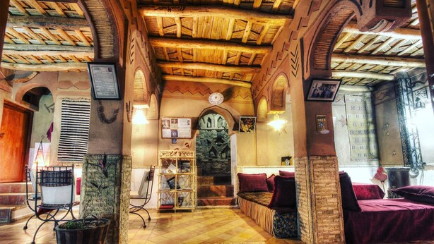 A cozy interior with a wooden ceiling, a stone pillar, a bookshelf, and a bed with a red blanket. - inn the Fibula of Dades (Boumalne Dadès)