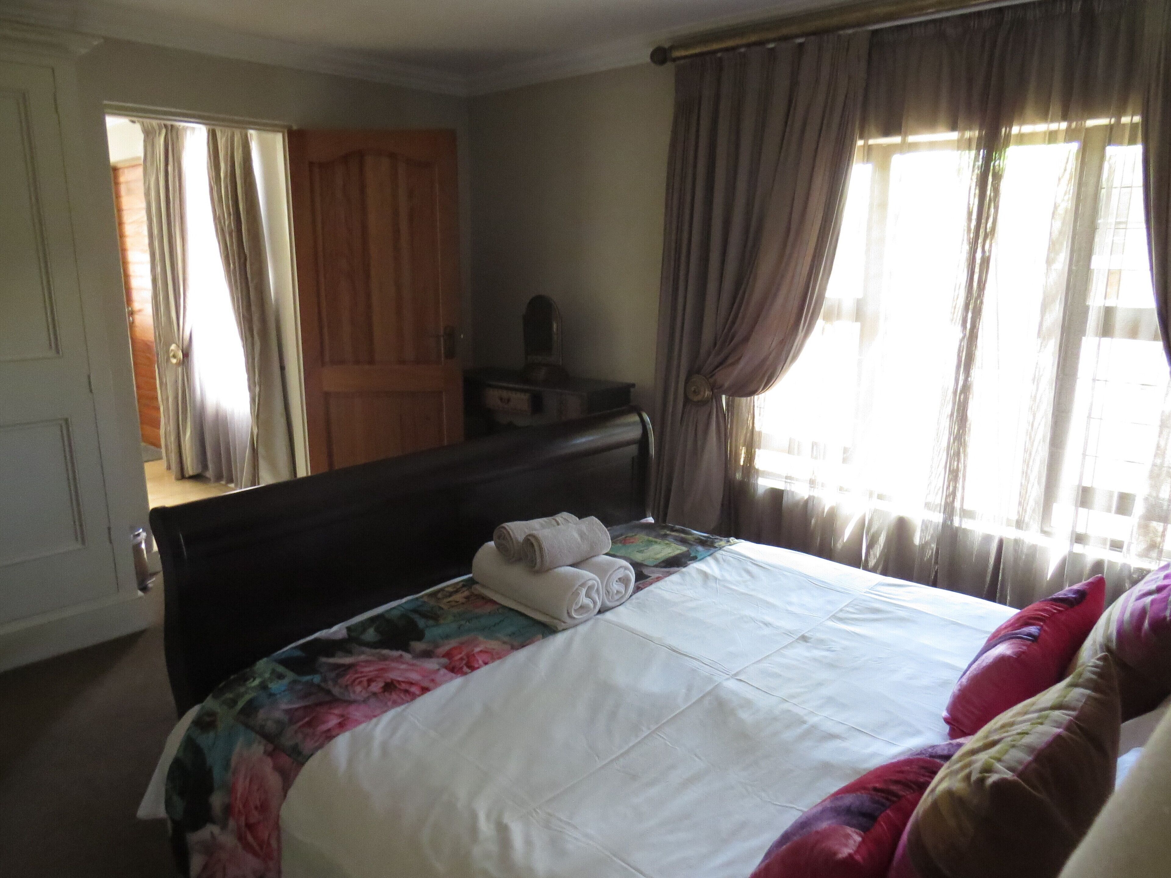 A bedroom with a bed, a dresser, a mirror, and a window with curtains.