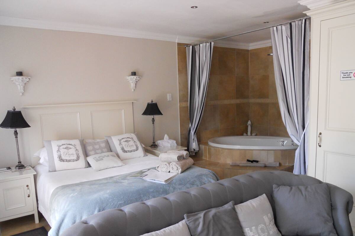 Une chambre d’hôtel comprenant un lit, un canapé, une salle de bain avec baignoire et un panneau indiquant qu’il est interdit de fumer.