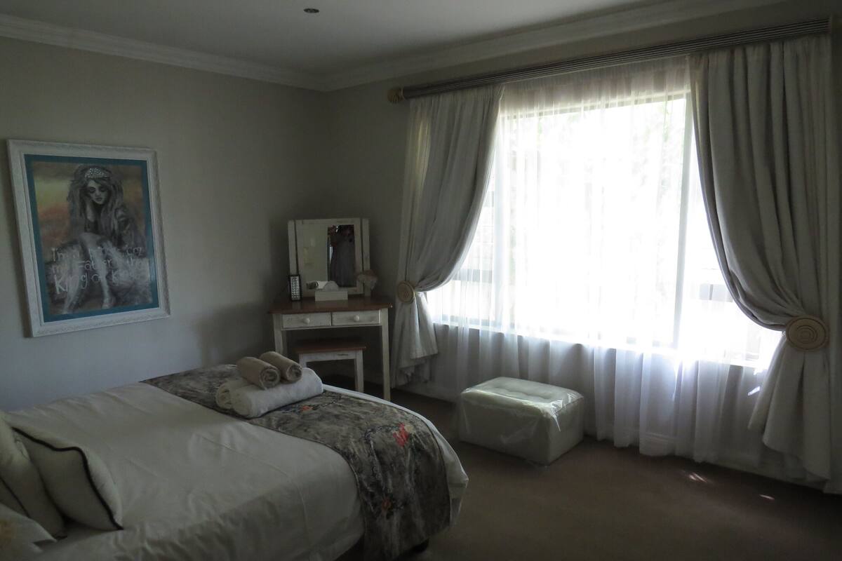 Une chambre à coucher avec un lit, une commode, un miroir et une fenêtre avec des rideaux.