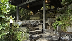 A traditional wooden structure with stone steps leading up to a covered area, surrounded by lush greenery. - Kurokawa Onsen Okunoyu (Minamioguni)