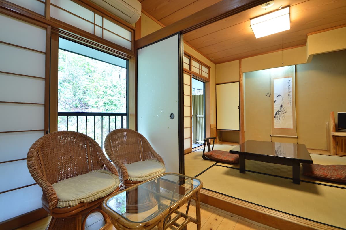 Ein traditioneller japanischer Raum mit Tatami-Böden, zwei Korbstühlen, einem niedrigen Tisch und Schiebetüren.