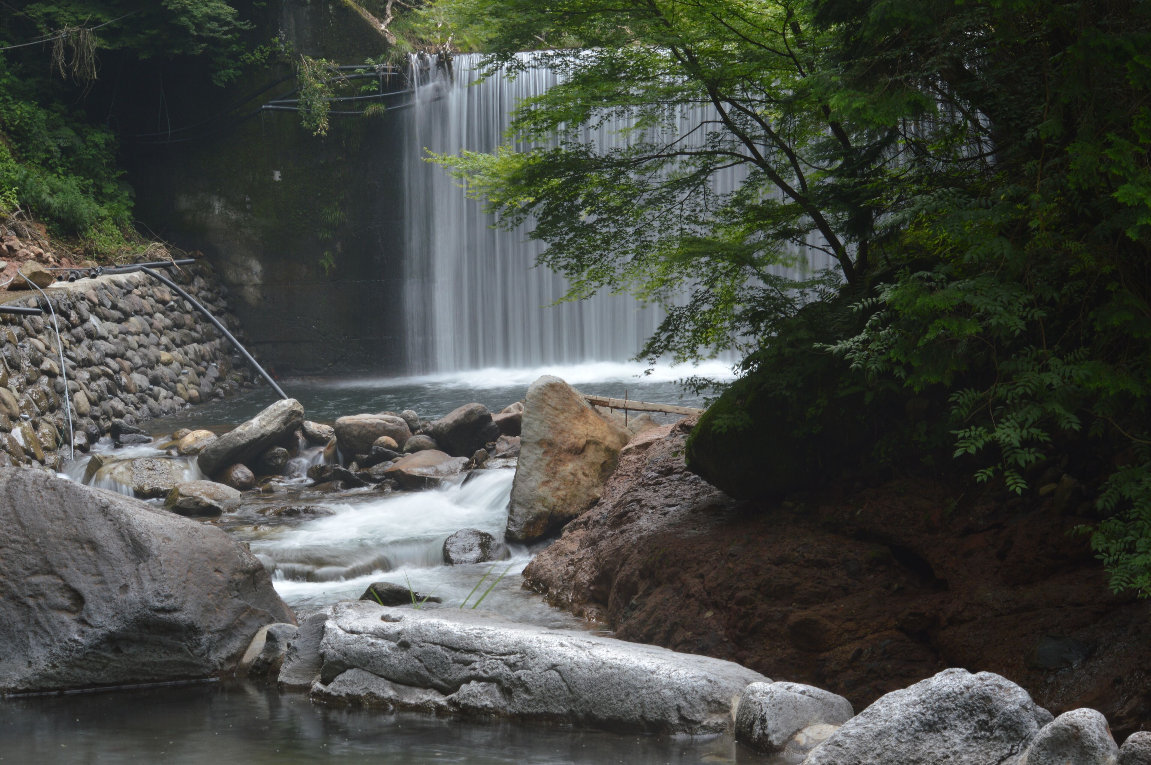 A waterfall cascading over rocks into a stream, surrounded by dense greenery.