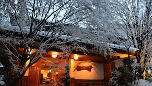 A traditional Japanese-style building with a wooden exterior, a stone entrance, and a snow-covered landscape. - Kurokawa Onsen Okunoyu (Minamioguni)